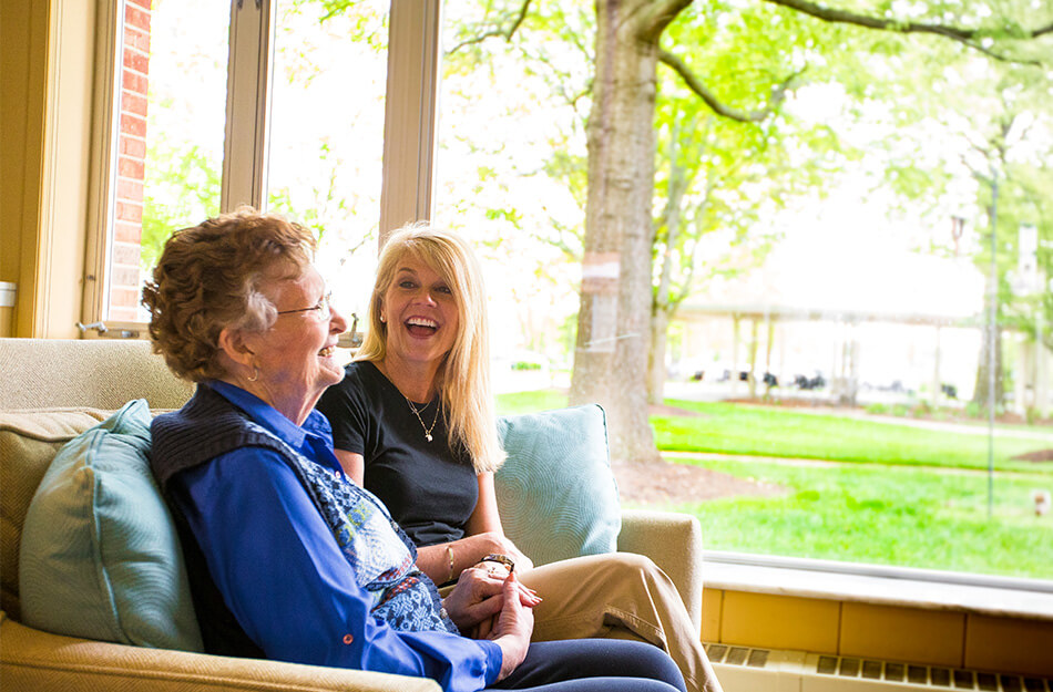 Senior woman and adult daughter sitting on the couch laughing
