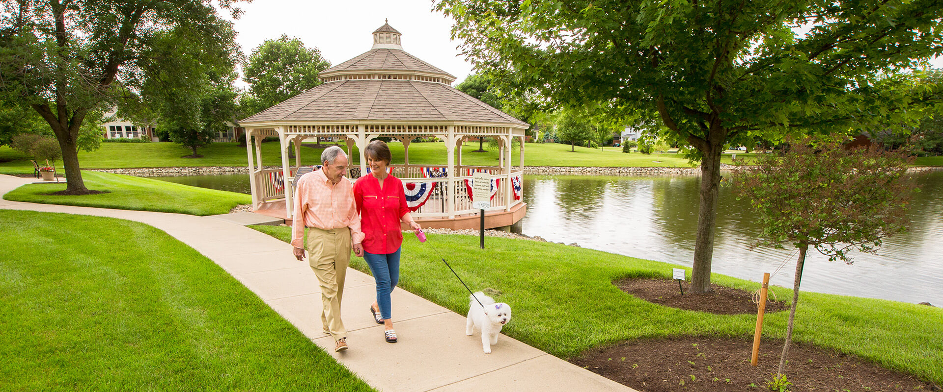 Senior couple walking white dog around pond