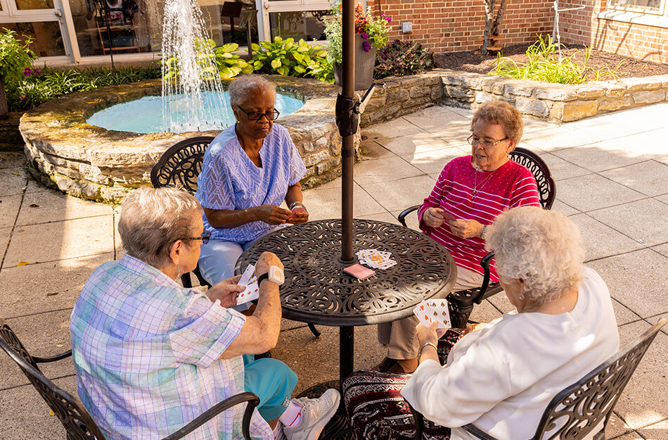 Senior friends sit around an outdoor table to play cards