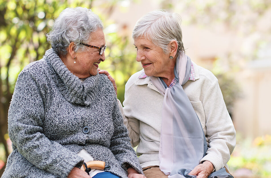 Senior friends laugh on garden bench