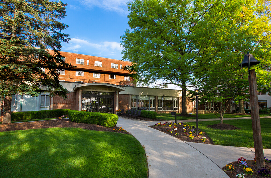 Exterior view of a red-brick senior living community with lush gardens and shady trees.