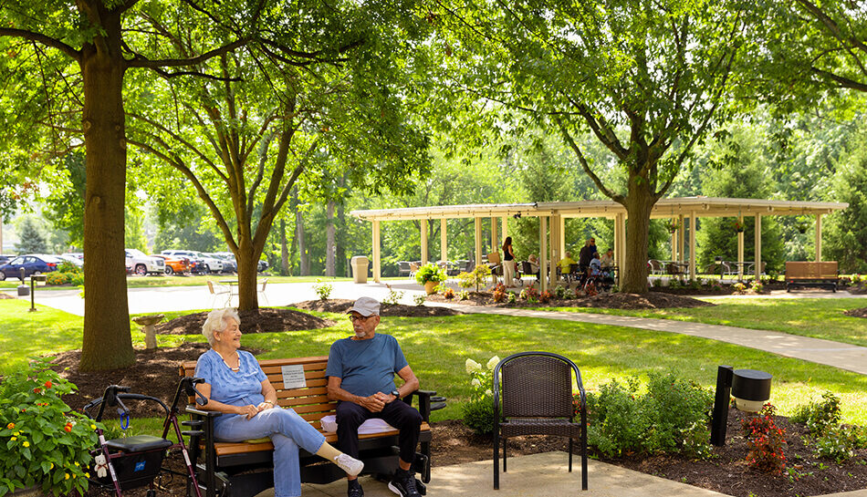 Older couple sitting on bench in shaded outdoor area at senior community.