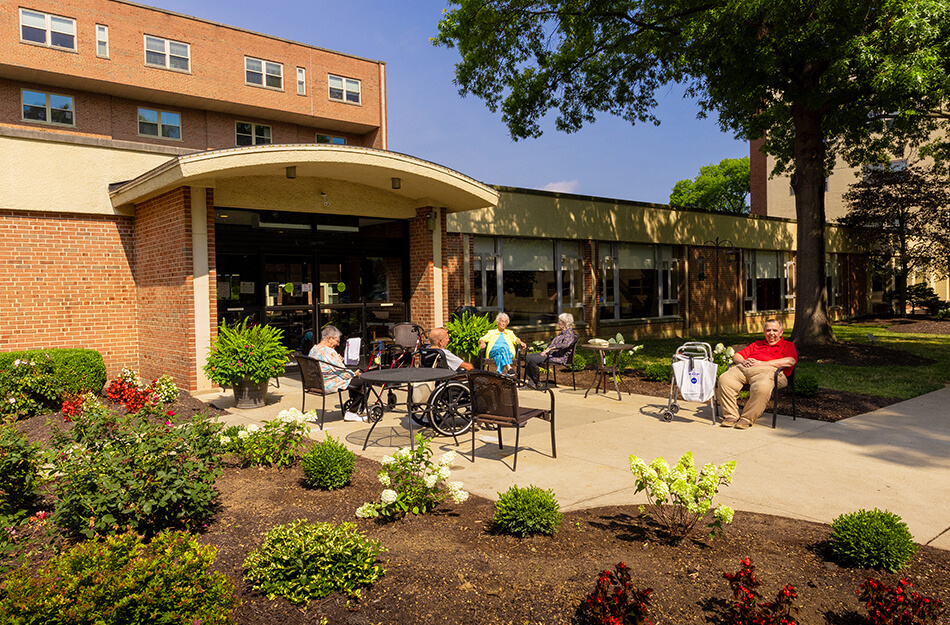 Residents relaxing outdoors at a senior living community on a sunny day.