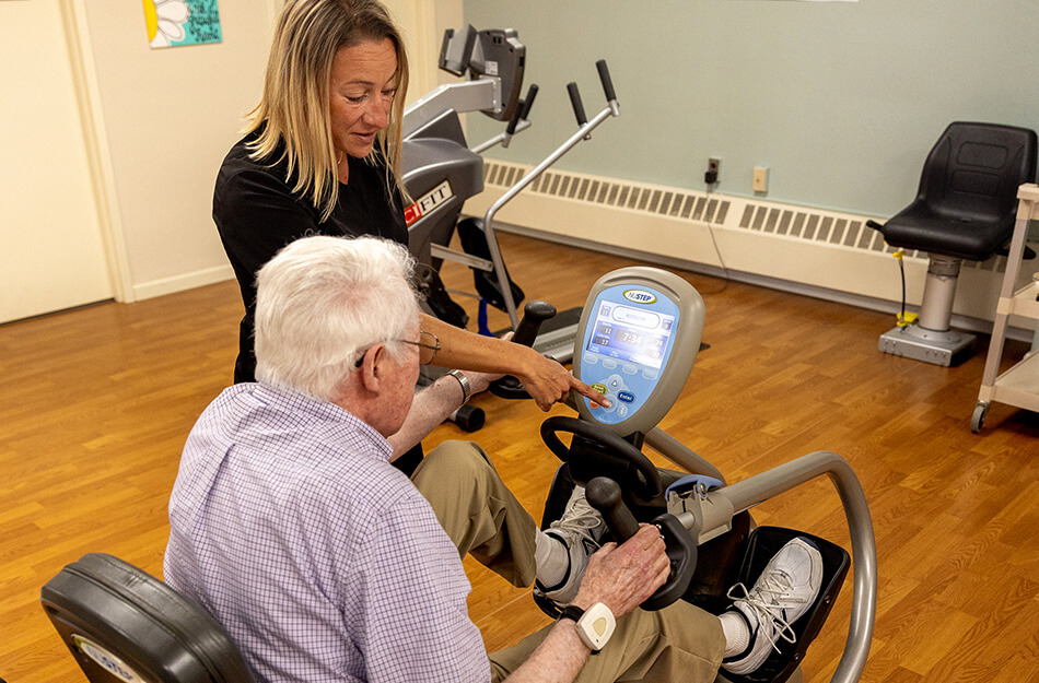 Senior man uses gym equipment with physical therapist