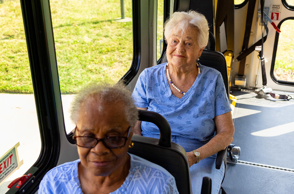 Two senior women sitting inside a bus, enjoying a community outing.