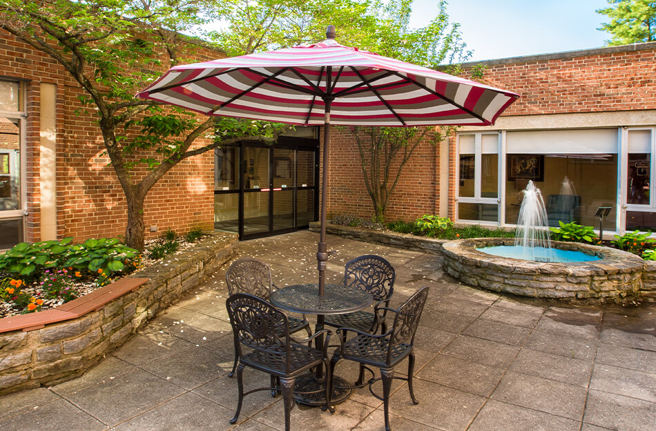 Courtyard with table, umbrella, and fountain in senior living community.
