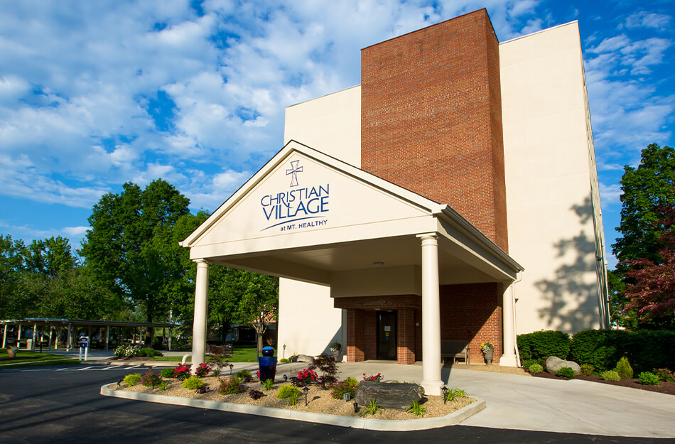Front entrance of a senior living community building with lush greenery.