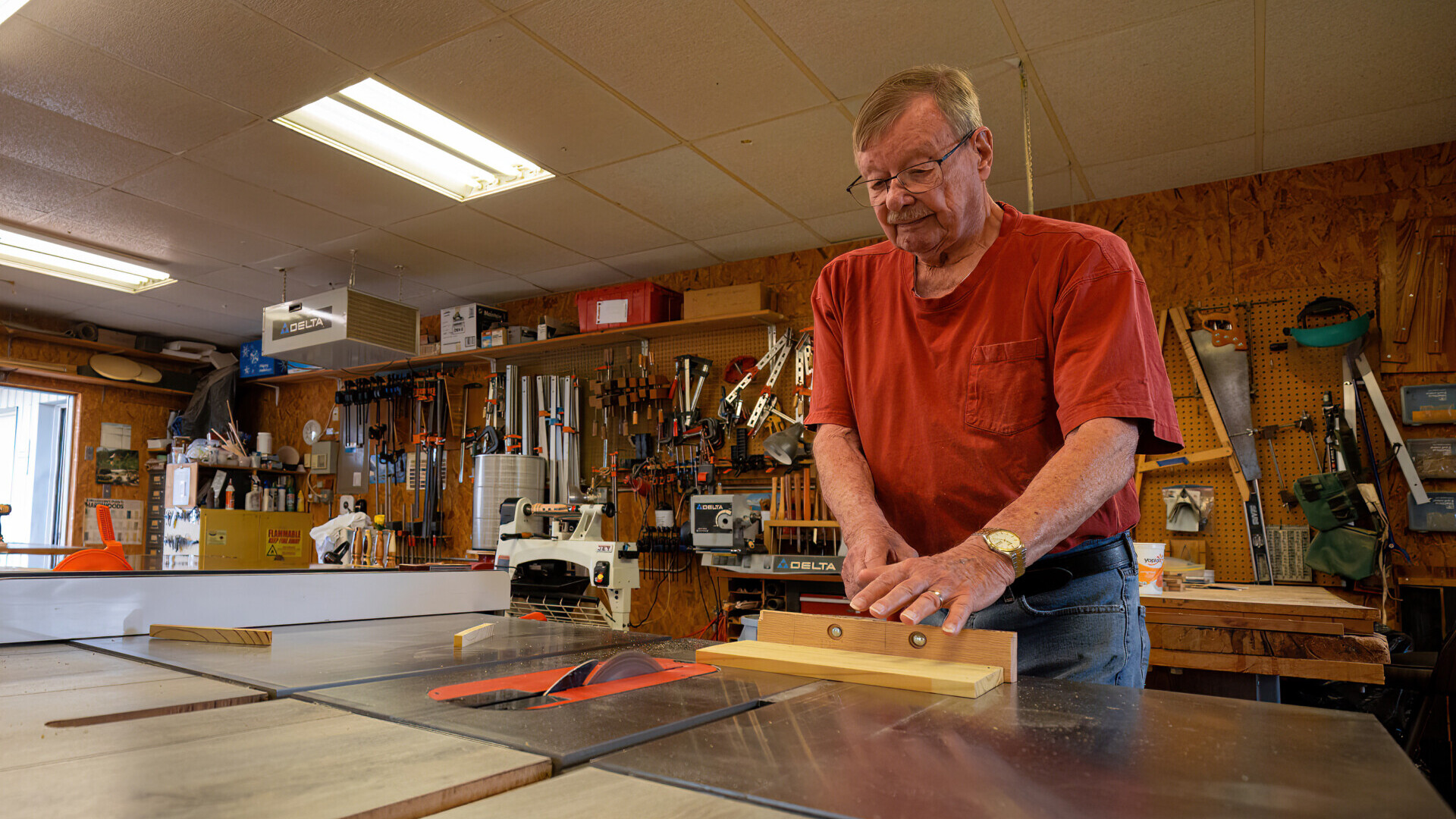 A man stands in a woodworking shop, preparing to cut a piece of wood on a table saw.