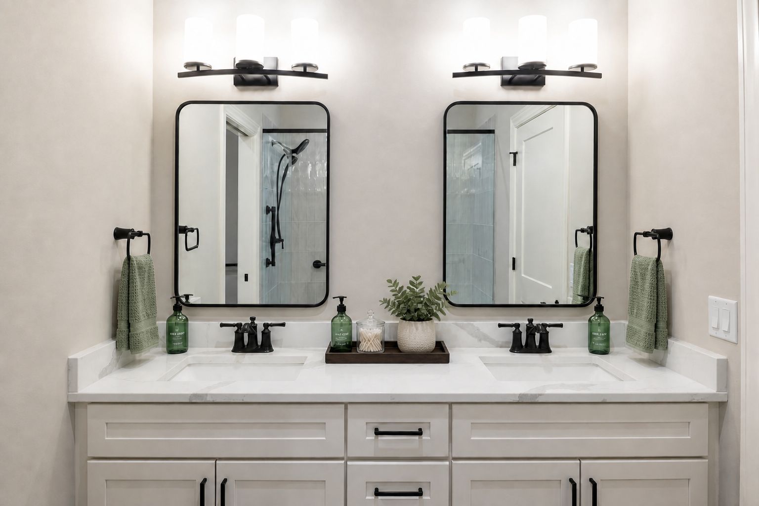 Interior shot of a modern bathroom vanity with marble countertop, double sinks, black fixtures, and premium finishes. In the reflection of the mirrors above each sink, a zero-entry shower with sliding glass doors is visible.